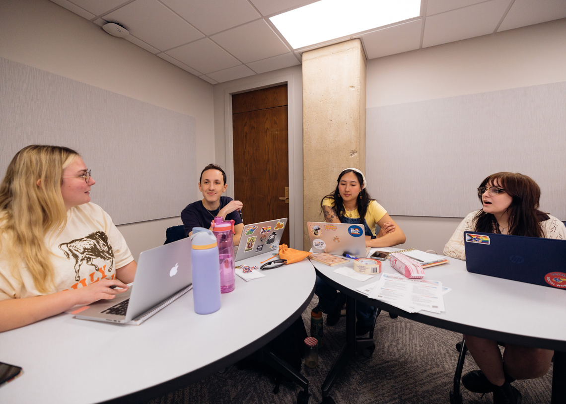 Four social work students talk at classroom tables at the KU School of Social Welfare